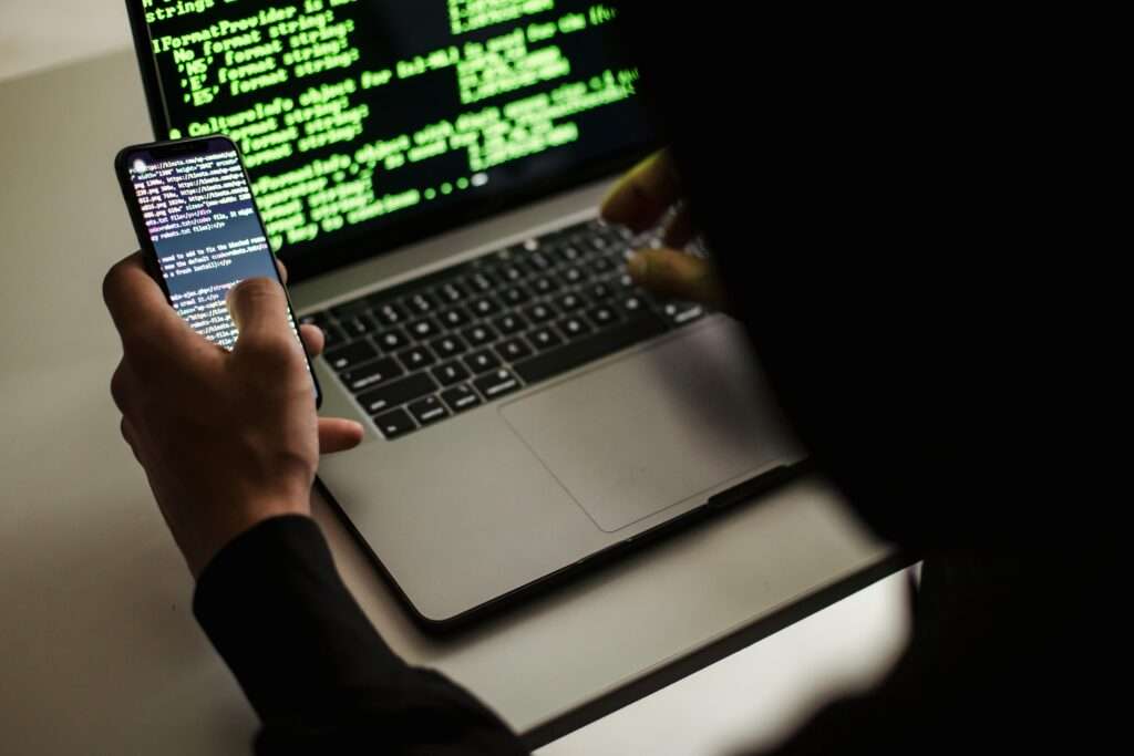 Fraude energético: los timos saltan de las llamadas telefónicas a los SMS de deudas falsas From behind crop male programmer in black hood browsing netbook and mobile phone while working in office